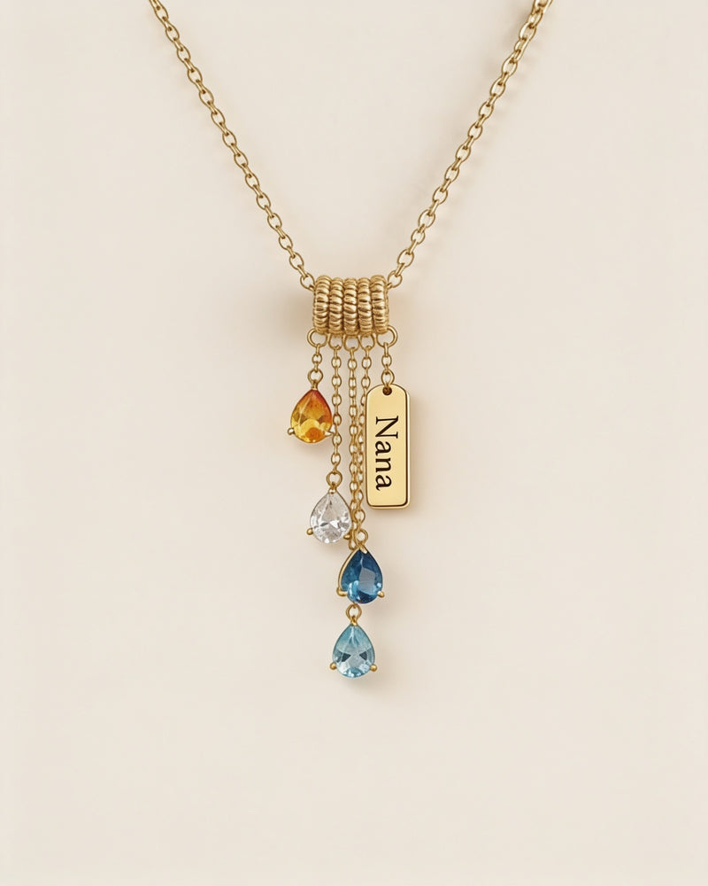 Gold cascading birthstone necklace with pear-cut stones and a small tag engraved Nana, hanging from a small coiled bar