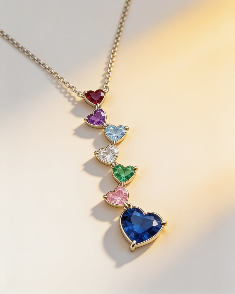 Birthstone Heart Cascade Necklace in gold with seven heart birthstones: garnet, amethyst, aquamarine, April clear stone, emerald, pink October stone and a sapphire-blue drop heart