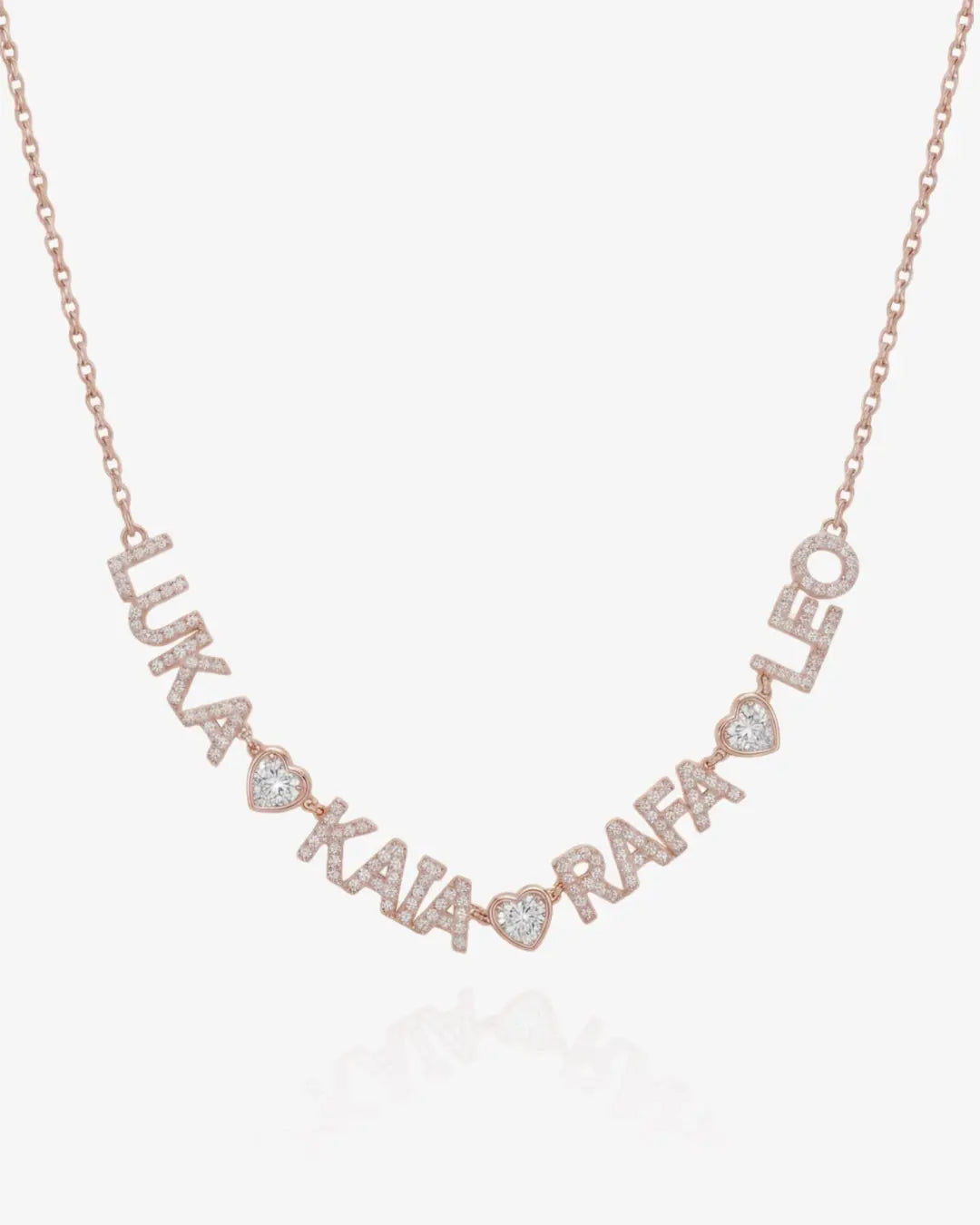 A rose gold personalized name necklace spelling out names with small heart-shaped accents and clear pavé stones, shown on a light gray background.