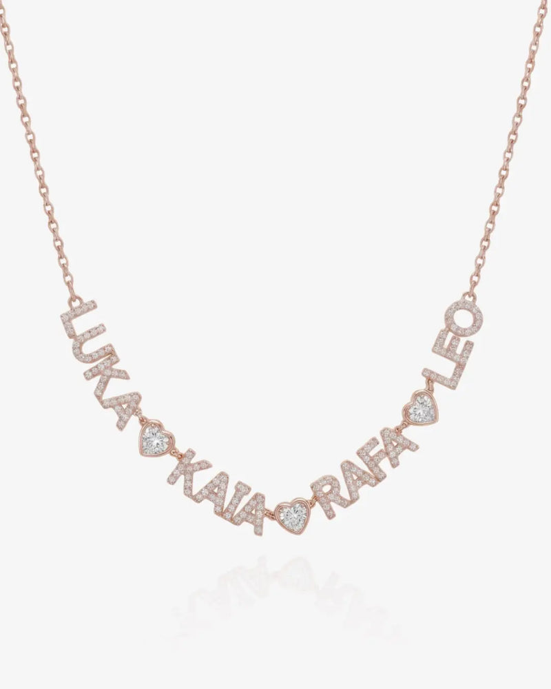 A rose gold personalized name necklace spelling out names with small heart-shaped accents and clear pavé stones, shown on a light gray background.